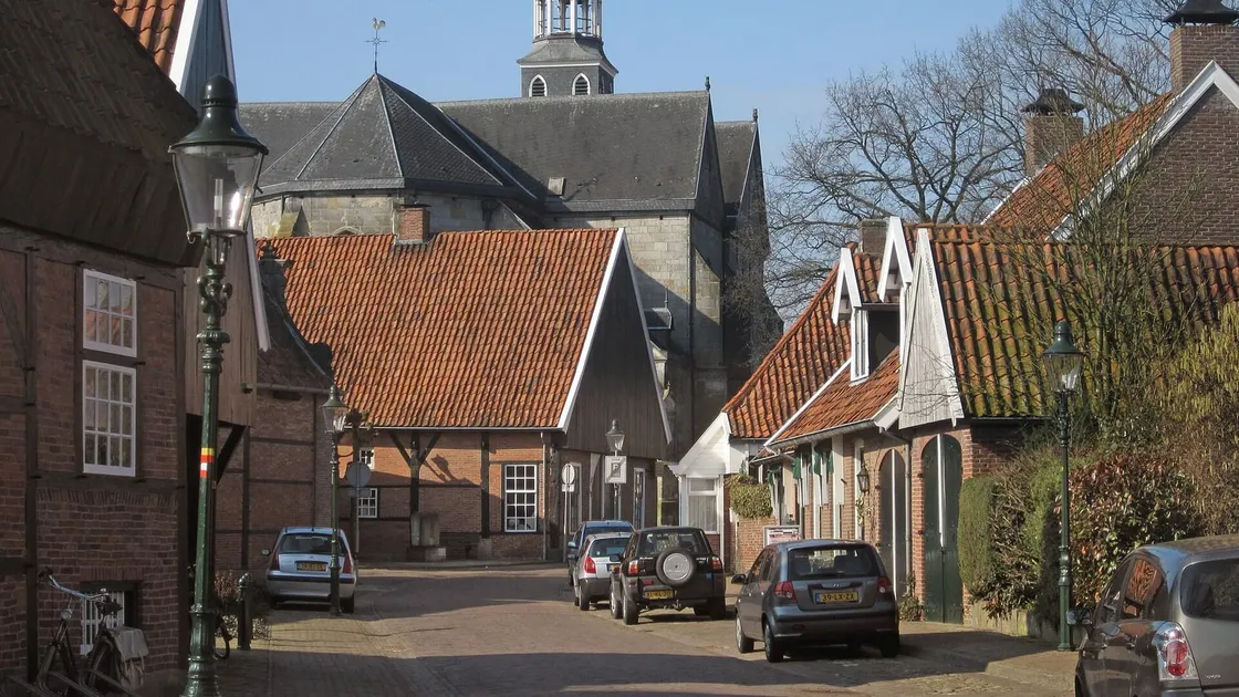 Straat met lage bakstenen huizen en rode pannendaken in Ootmarsum, met daarachter de toren van de kerk.